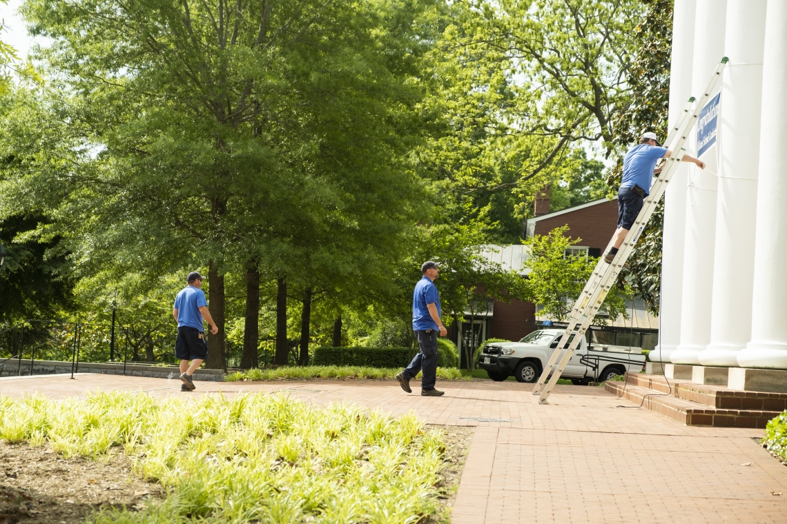 (L-R): Todd Stinnett and Michael Rhodenizer look on as James Cauley hangs a Williams School sign for graduation. Stinnett and Cauley are carpenters and Rhodenizer is a lead carpenter in University Facilities.