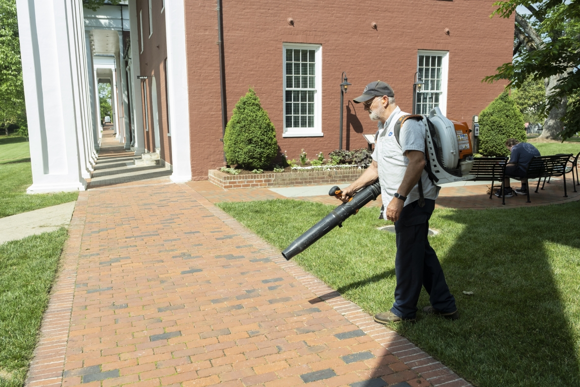 Grounds Worker Larry Hostetter blows grass clippings off the sidewalk next to the Colonnade.
